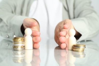 Photo of Financial inequality. Woman moving wooden figures and different stacks of coins away from each other at white table, closeup