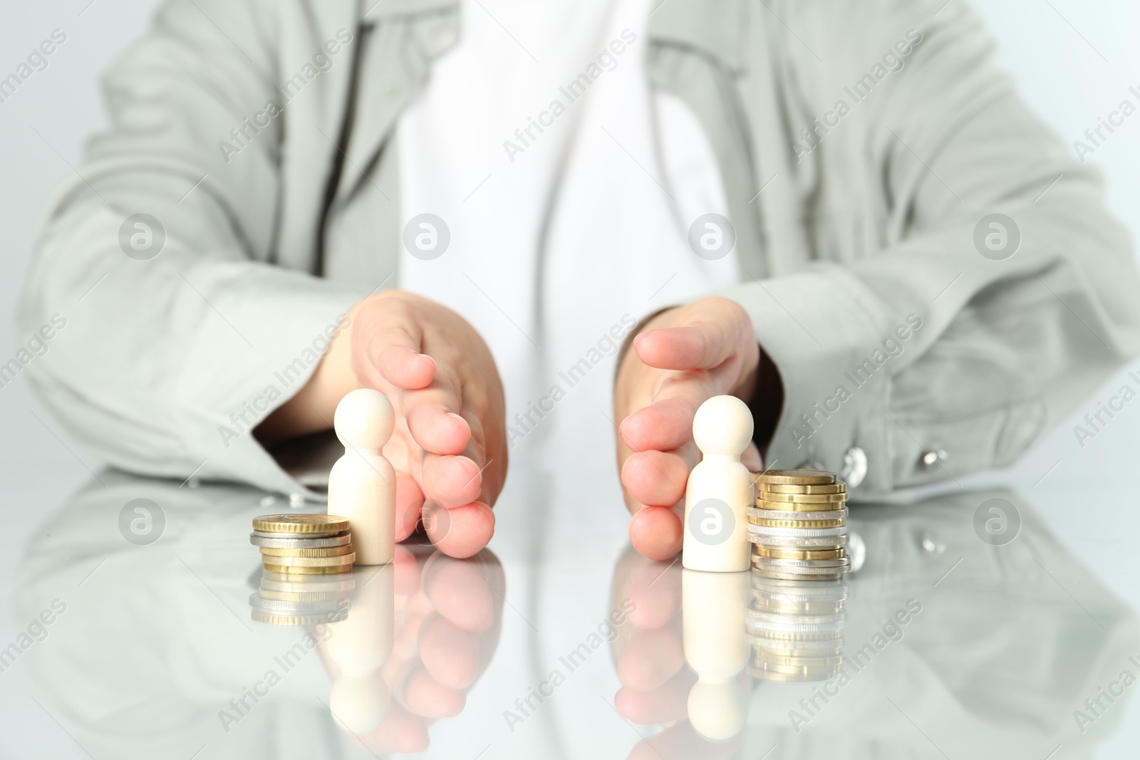 Photo of Financial inequality. Woman moving wooden figures and different stacks of coins away from each other at white table, closeup