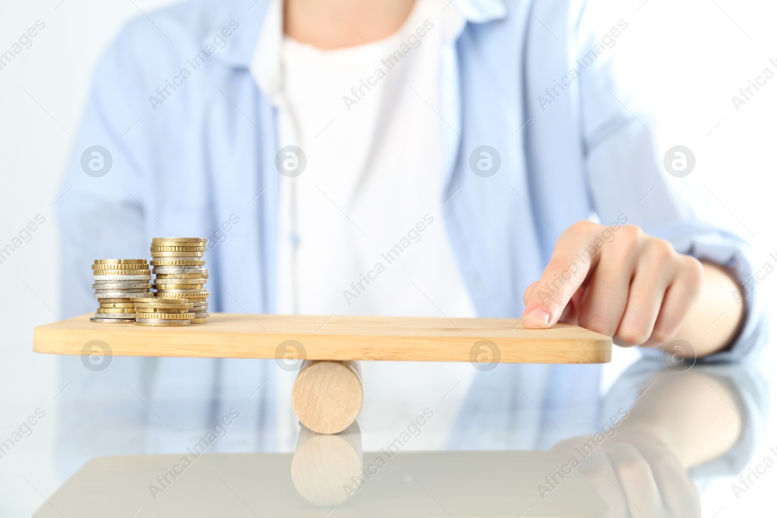 Photo of Financial inequality. Woman balancing wooden seesaw with stacks of coins at white table, closeup