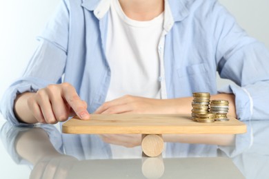 Photo of Financial inequality. Woman balancing wooden seesaw with stacks of coins at white table, closeup