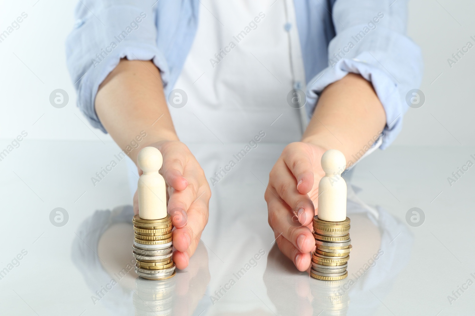 Photo of Financial equality. Woman moving stacks of coins and wooden figures away from each other at white table, closeup