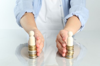 Financial equality. Woman moving stacks of coins and wooden figures away from each other at white table, closeup