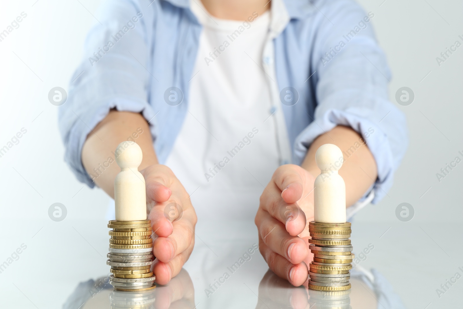 Photo of Financial equality. Woman moving stacks of coins and wooden figures away from each other at white table, closeup