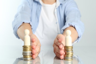 Photo of Financial equality. Woman moving stacks of coins and wooden figures away from each other at white table, closeup