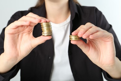 Photo of Financial inequality. Woman comparing two stacks of coins on white background, closeup