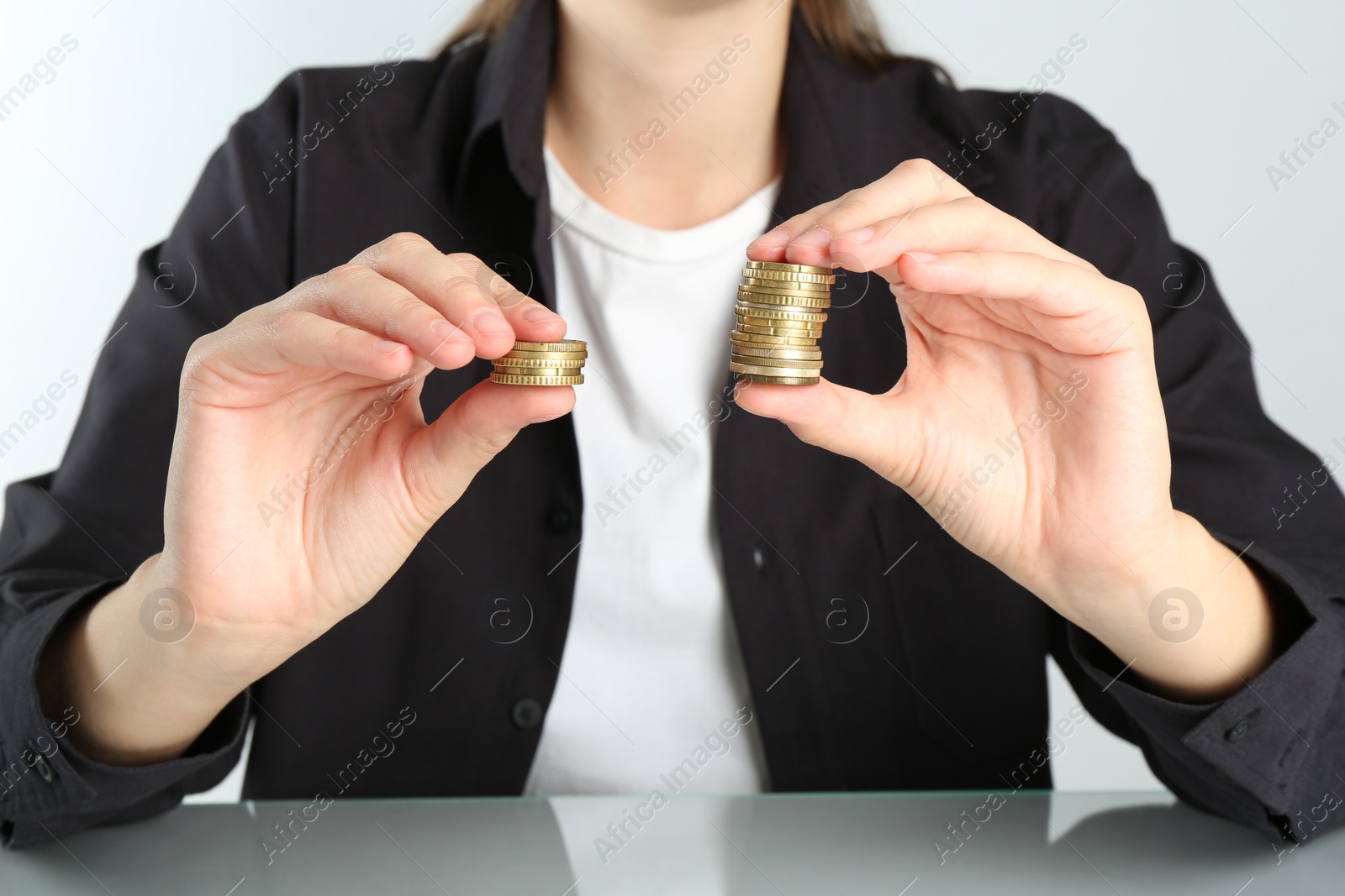 Photo of Financial inequality. Woman comparing two stacks of coins at table, closeup