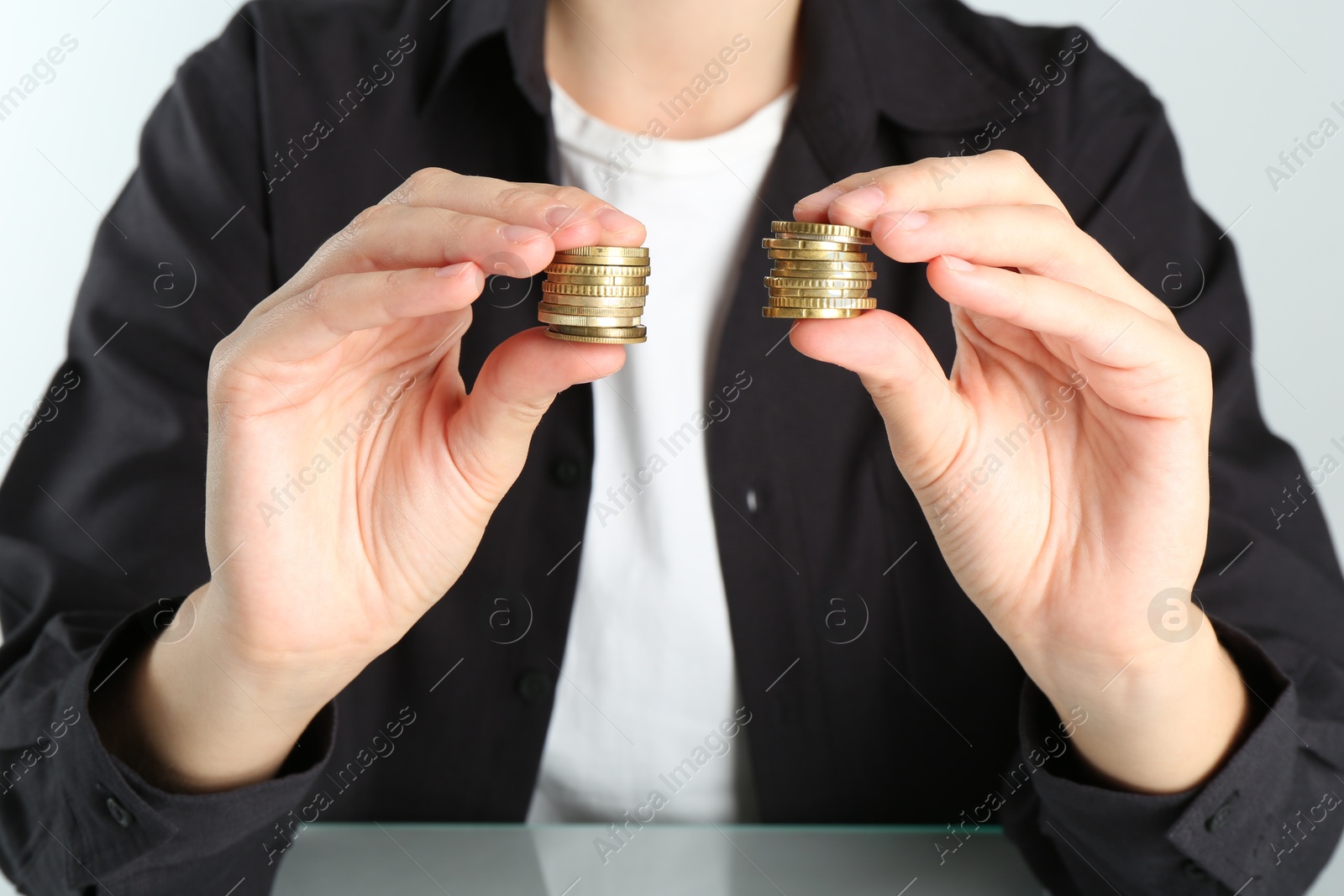 Photo of Financial equality. Woman comparing two stacks of coins at table, closeup