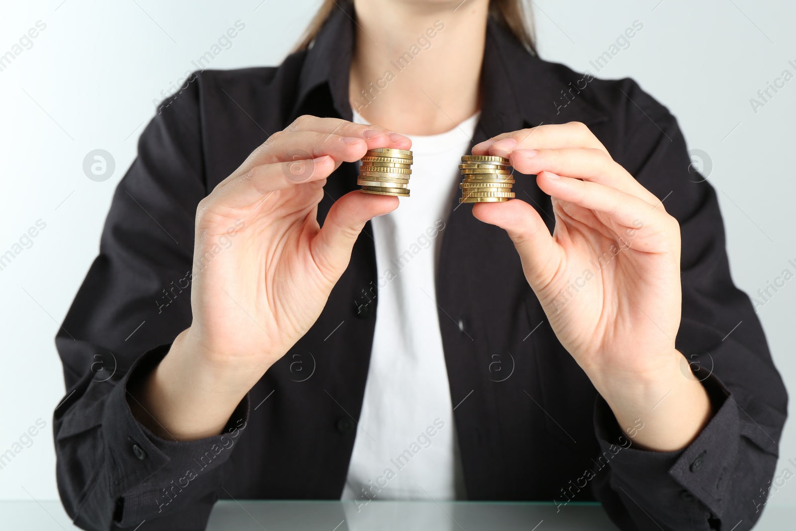 Photo of Financial equality. Woman comparing two stacks of coins at table, closeup