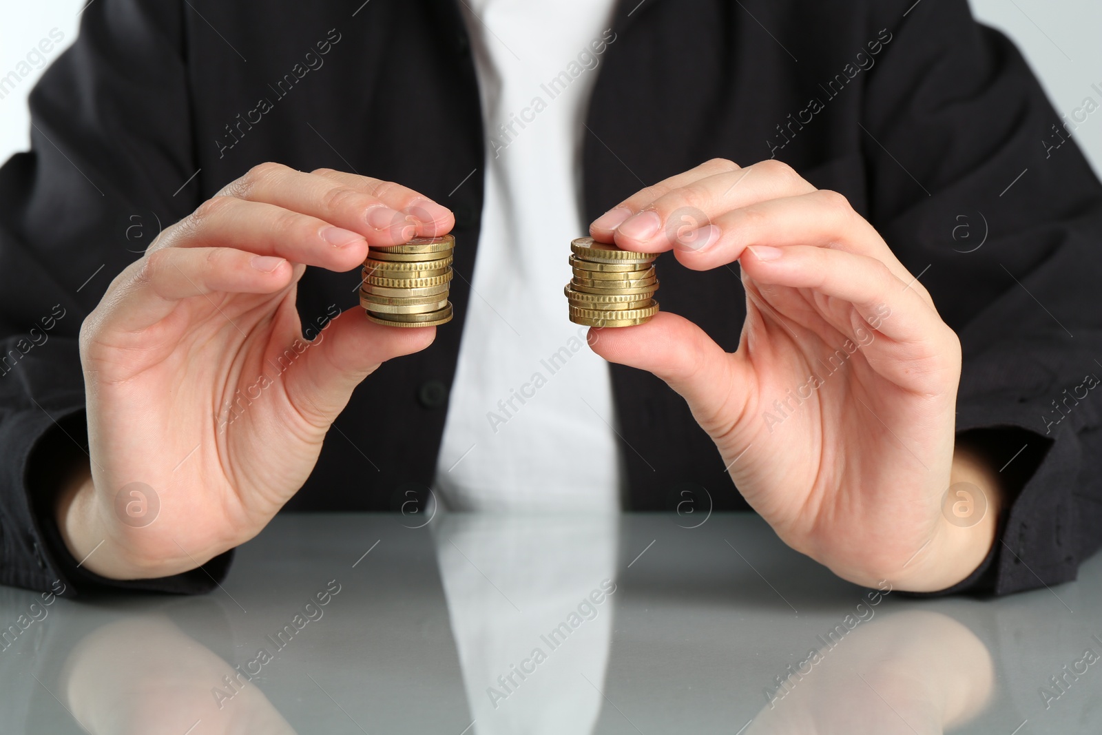 Photo of Financial equality. Woman comparing two stacks of coins at table, closeup