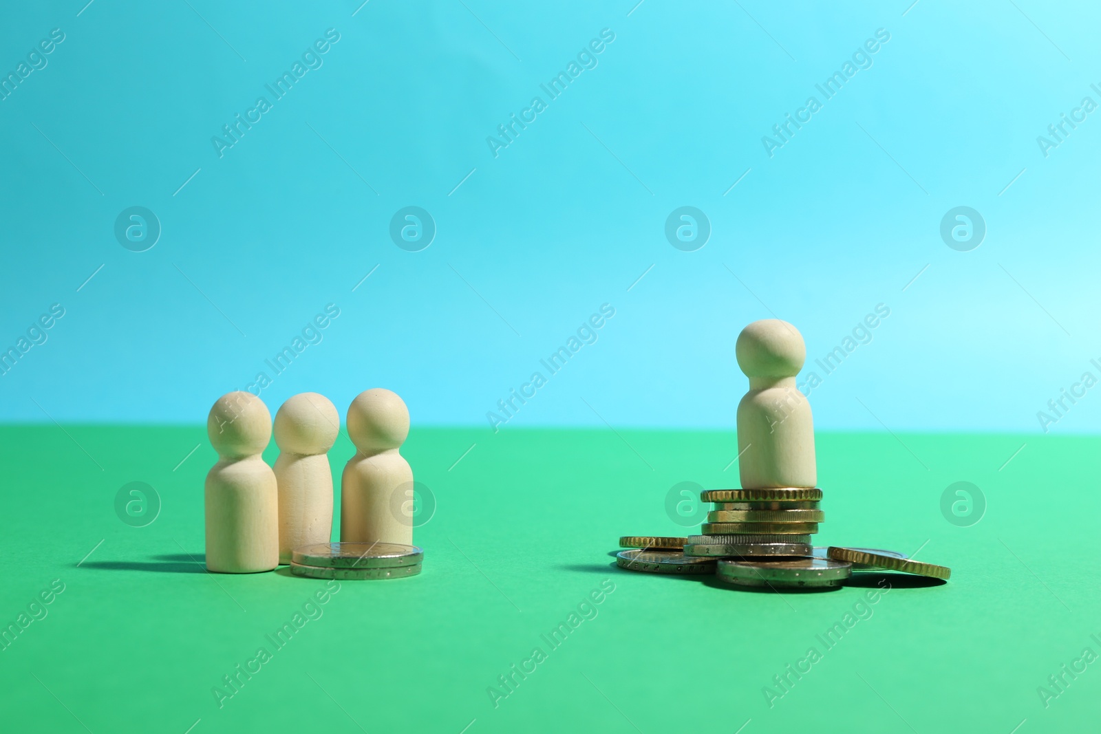 Photo of Financial inequality. One wooden figure on bigger stack of coins than others against light blue background. Space for text