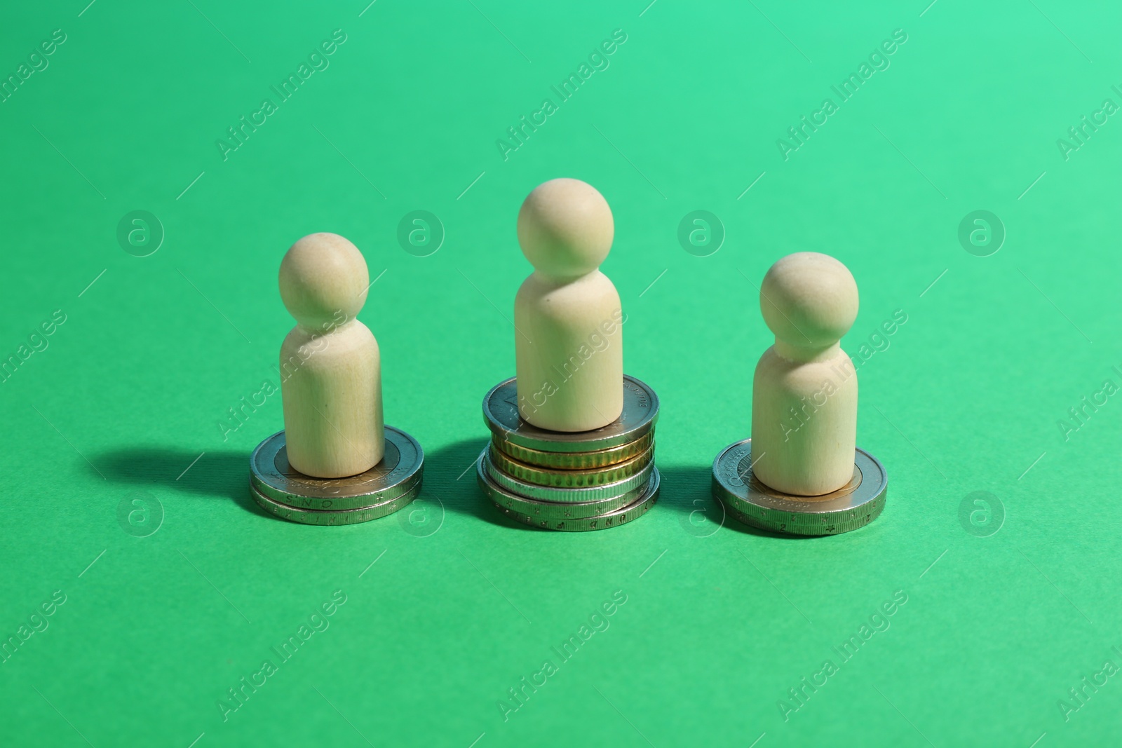 Photo of Financial inequality. Wooden figures on stacked coins of different height on green background