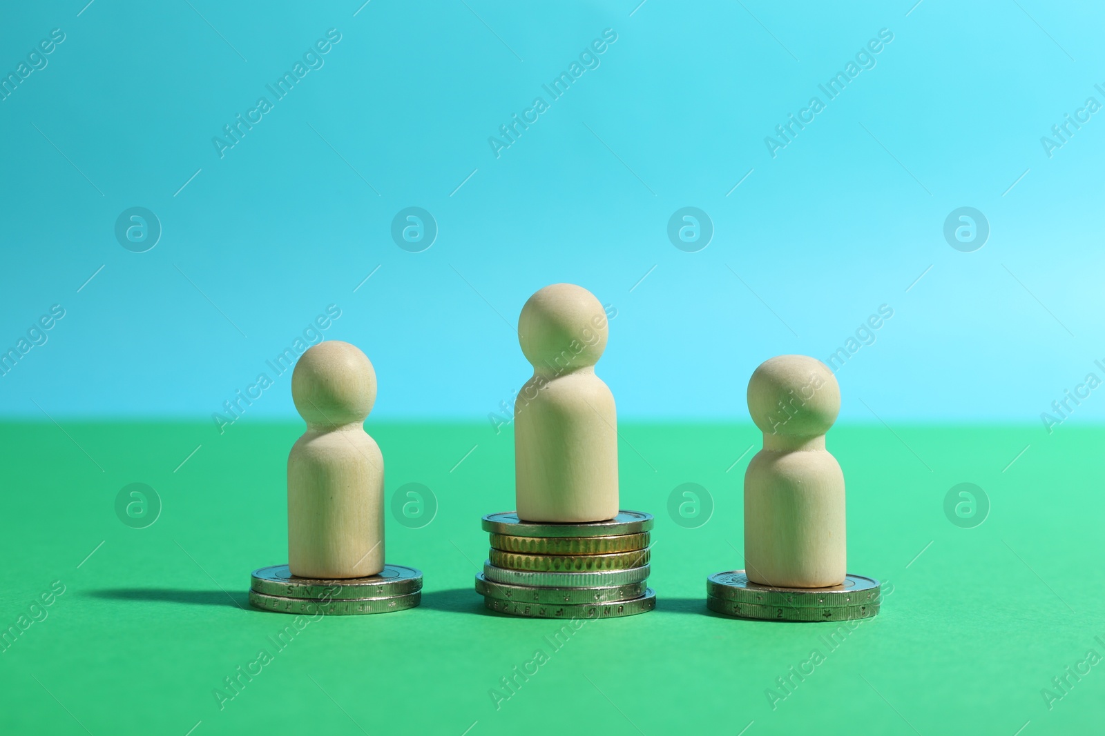 Photo of Financial inequality. Wooden figures on stacked coins of different height on green background