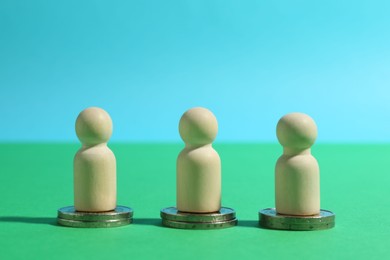 Financial equality. Wooden figures with stacked coins on color background