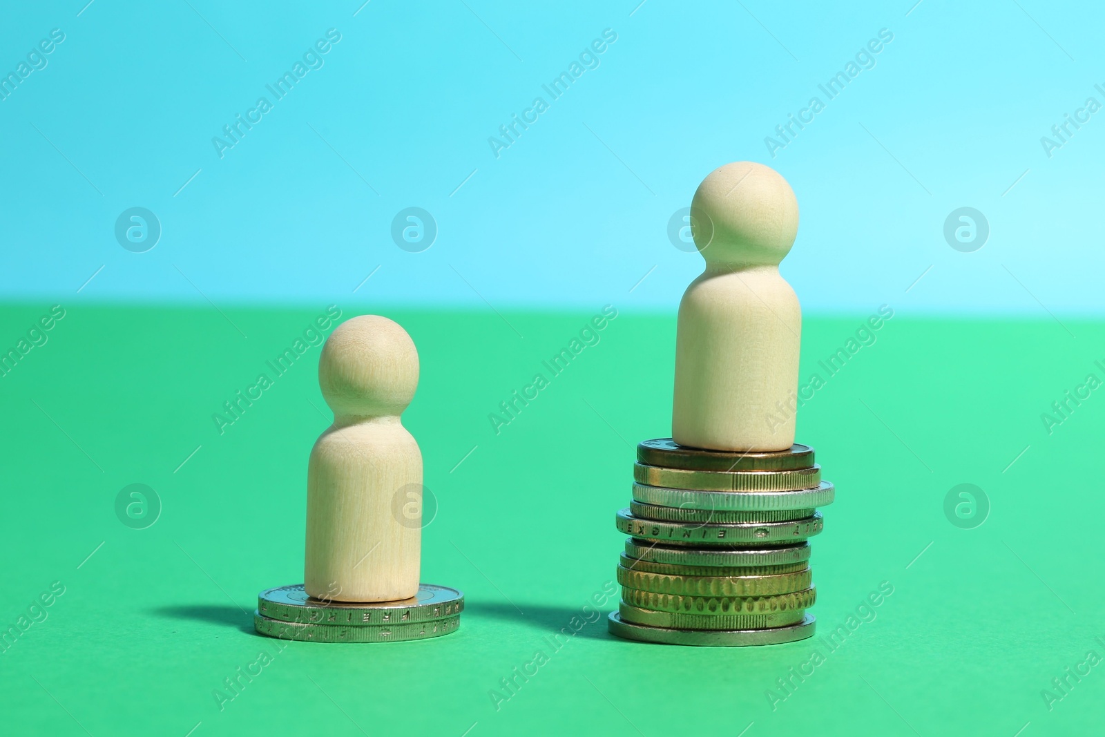 Photo of Financial inequality. One wooden figure on bigger stack of coins than another on color background