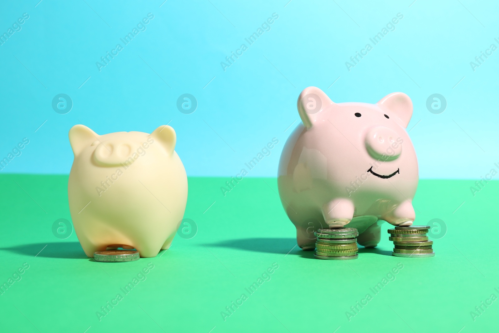 Photo of Financial inequality. One piggy bank with bigger stack of coins than another on color background