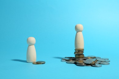 Financial inequality. One wooden figure on bigger stack of coins than another on light blue background