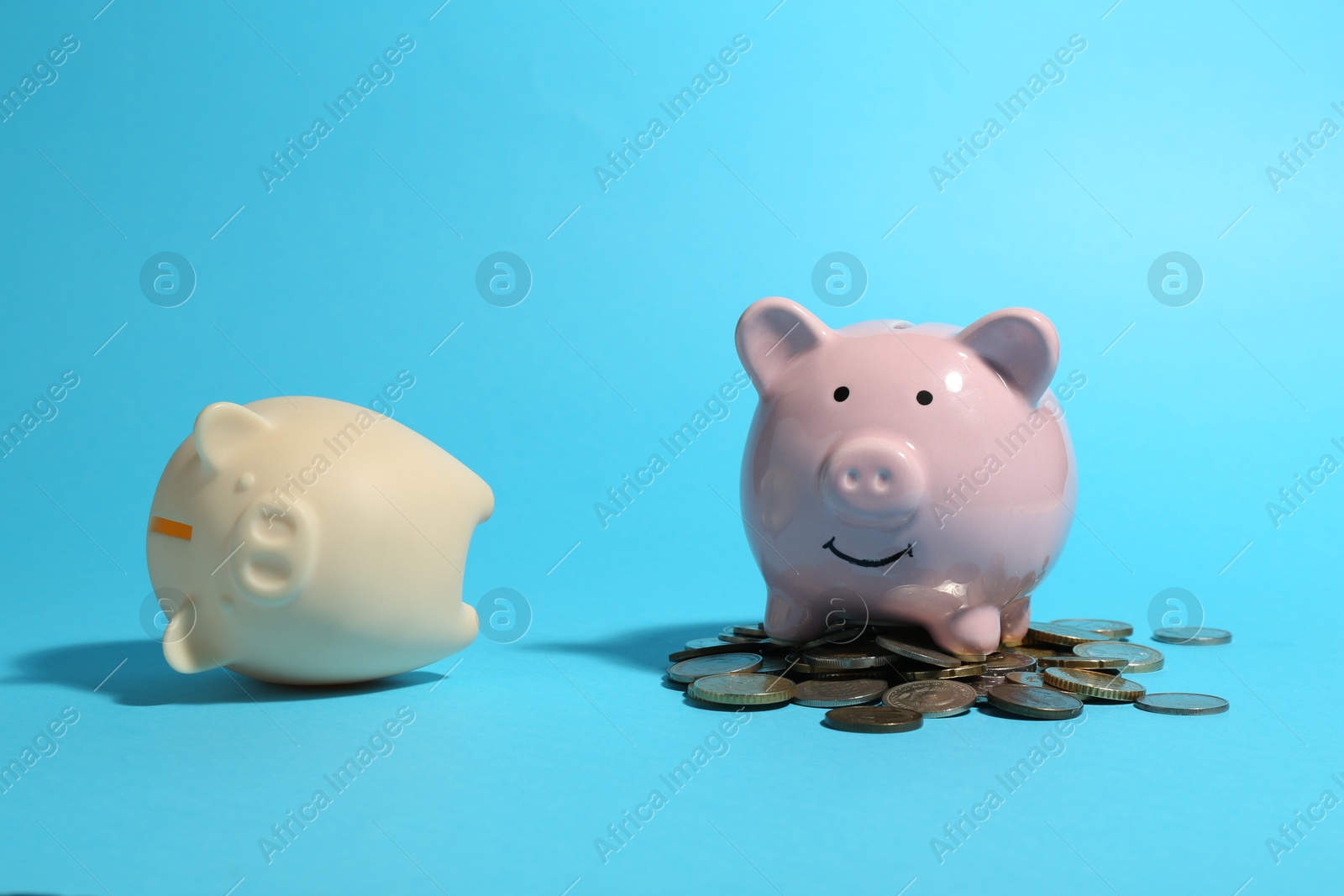 Photo of Financial inequality. Piggy bank with coins and empty one on light blue background