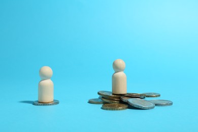 Photo of Financial inequality. One wooden figure on bigger pile of coins than another on light blue background