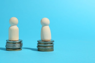 Financial equality. Wooden figures on similar stacks of coins on light blue background. Space for text