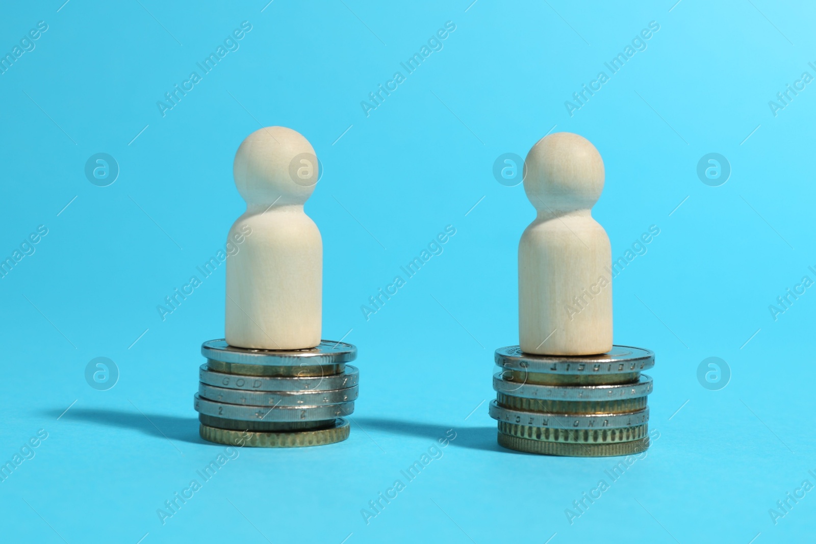 Photo of Financial equality. Wooden figures on similar stacks of coins on light blue background