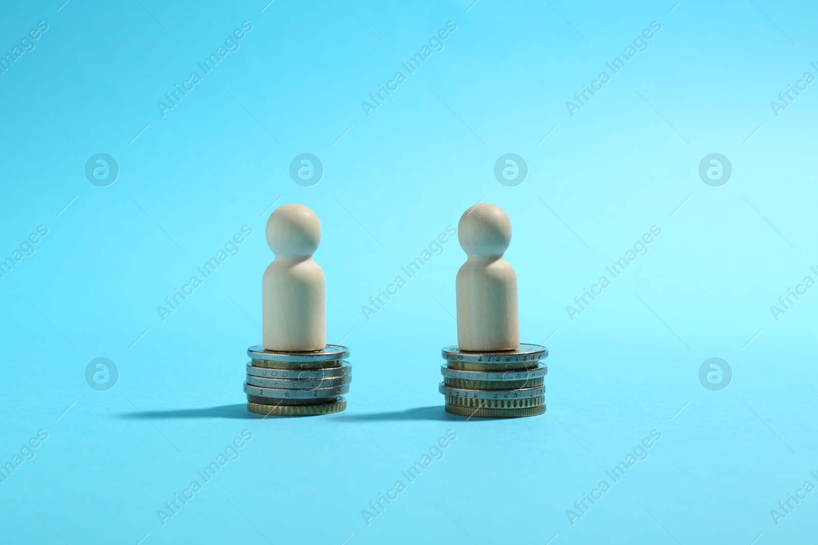 Photo of Financial equality. Wooden figures on similar stacks of coins on light blue background