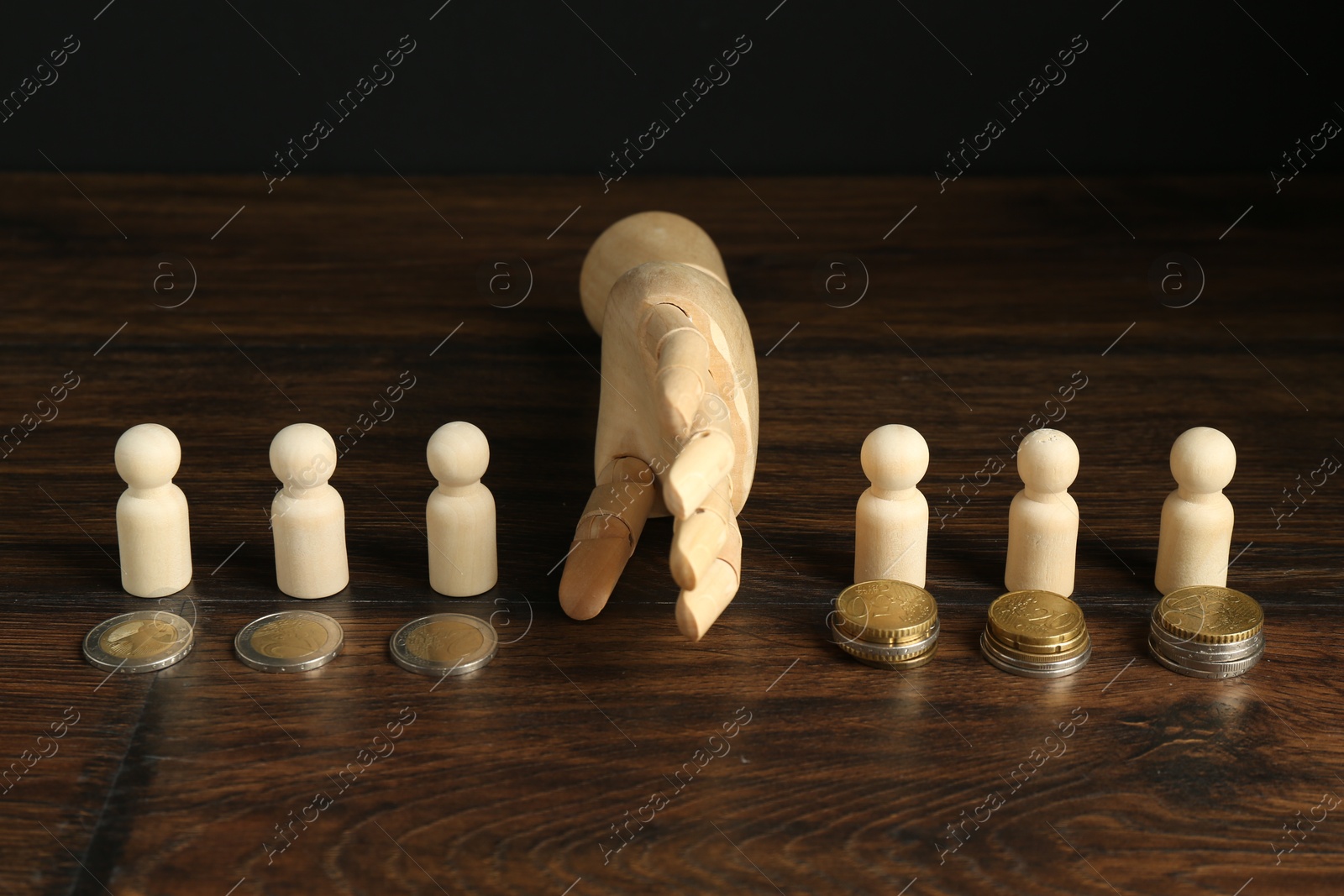 Photo of Financial inequality. Mannequin hand dividing wooden figures by theirs quantity of coins on table