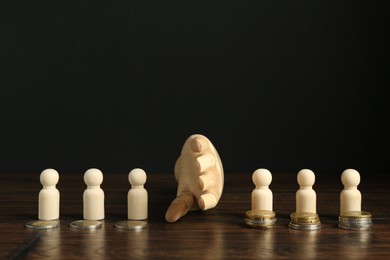 Photo of Financial inequality. Mannequin hand dividing wooden figures by theirs quantity of coins on table. Space for text