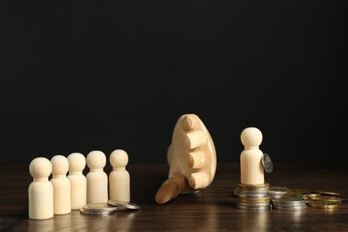 Photo of Financial inequality. Mannequin hand separating wooden figure from others by theirs quantity of coins on table