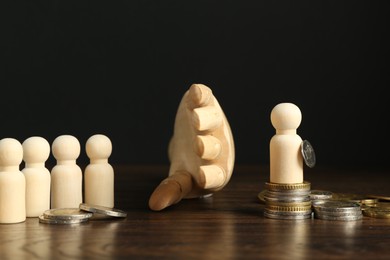 Photo of Financial inequality. Mannequin hand separating wooden figure from others by theirs quantity of coins on table