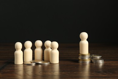 Financial inequality. Wooden figure with more coins than others on table