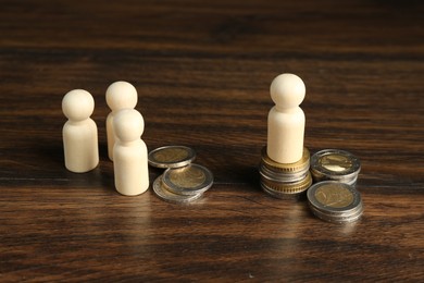 Financial inequality. Wooden figure with more coins than others on table