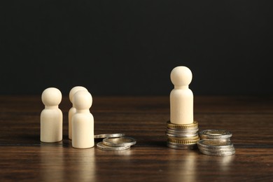 Financial inequality. Wooden figure with more coins than others on table