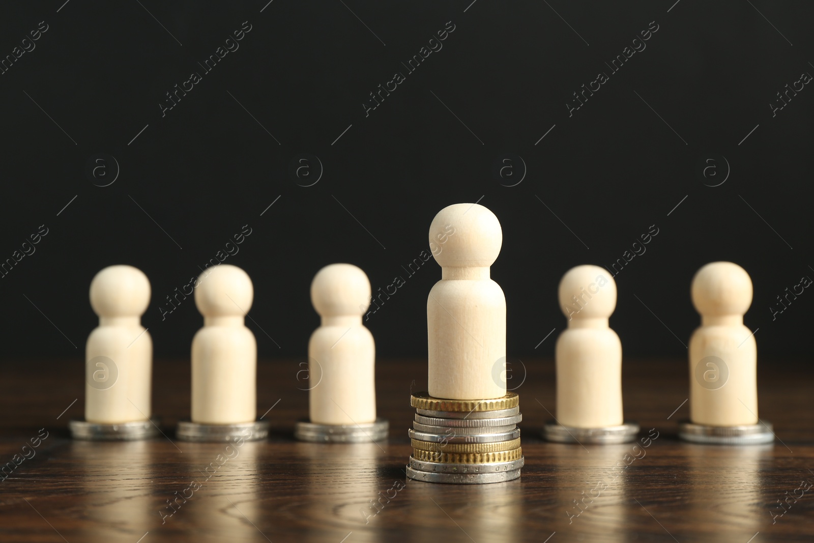 Photo of Financial inequality. One wooden figure with bigger stack of coins than others on table