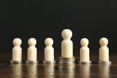 Financial inequality. One wooden figure with bigger stack of coins than others on table