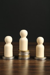 Photo of Financial inequality. One wooden figure with bigger stack of coins than others on table