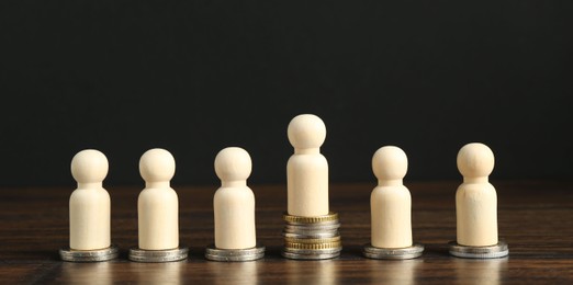 Financial inequality. One wooden figure with bigger stack of coins than others on table. Banner design