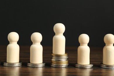 Photo of Financial inequality. One wooden figure with bigger stack of coins than others on table