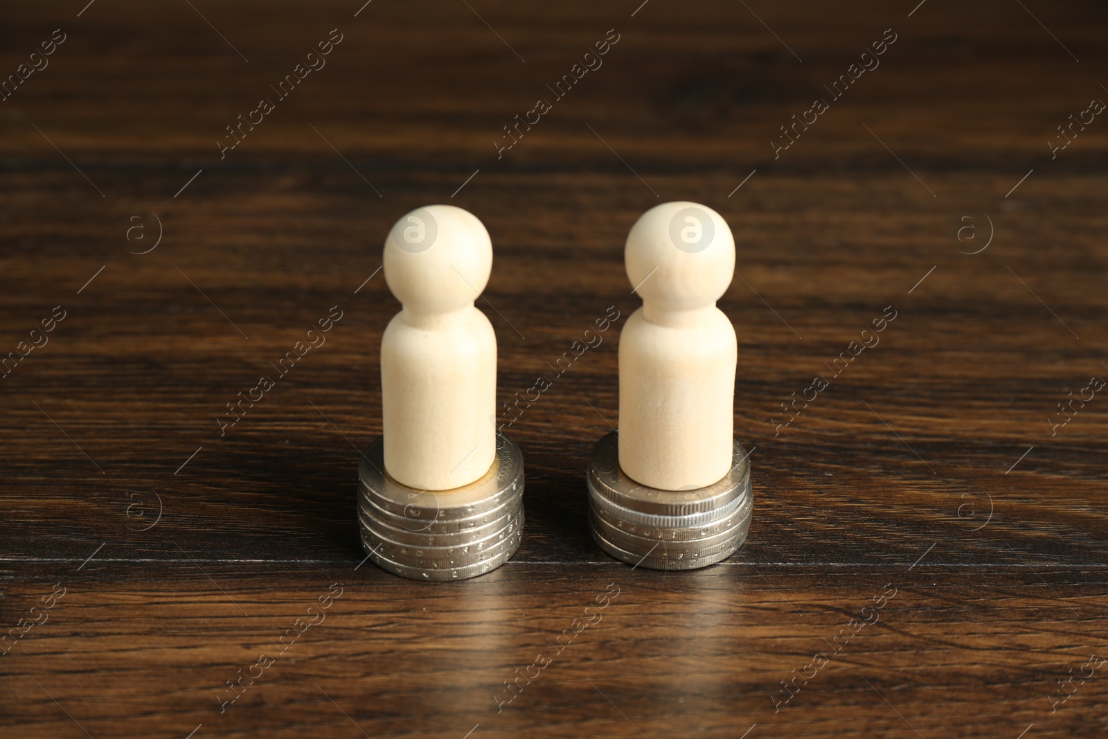 Photo of Financial equality. Wooden figures with similar quantity of coins on table