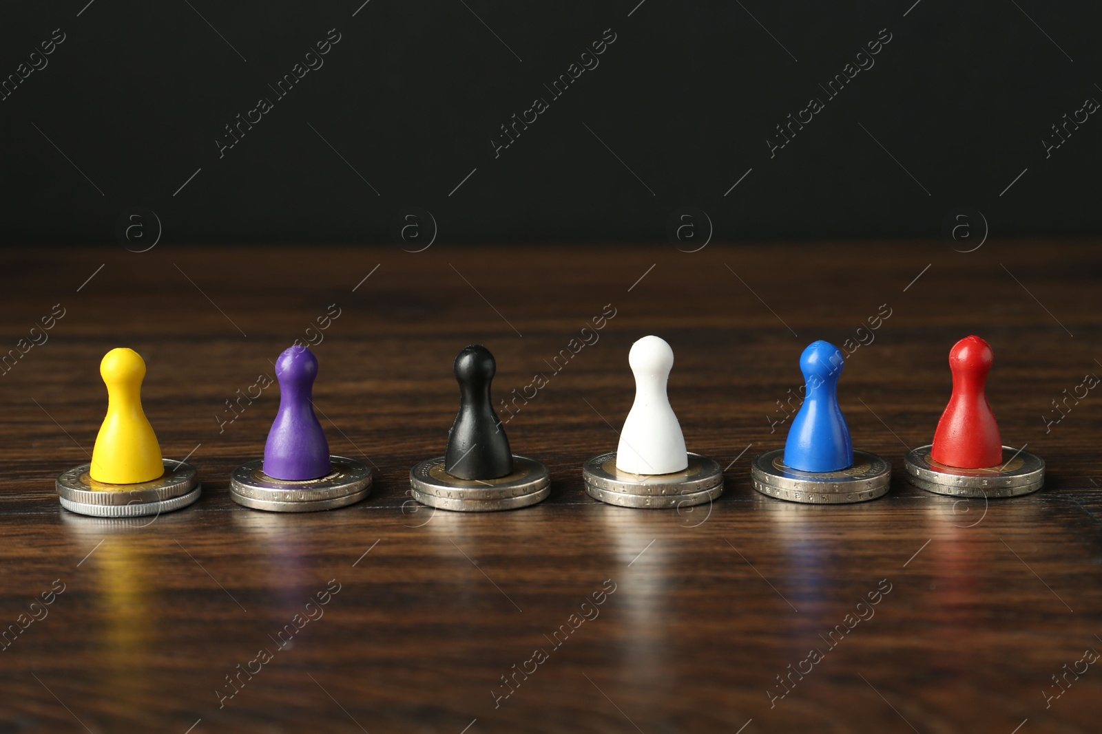 Photo of Financial equality. Colorful game pieces with similar quantity of coins on wooden table