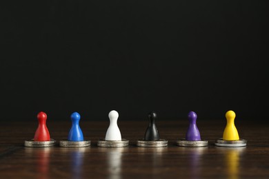 Photo of Financial equality. Colorful game pieces with similar quantity of coins on wooden table. Space for text