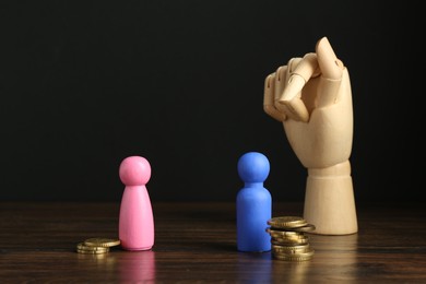 Photo of Financial inequality. Male and female figures with uneven amount of coins and mannequin hand on wooden table