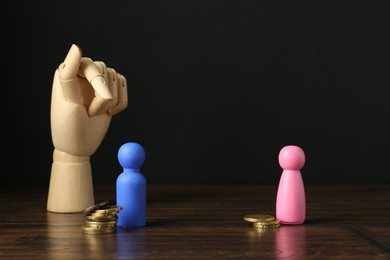 Financial inequality. Male and female figures with uneven amount of coins and mannequin hand on wooden table