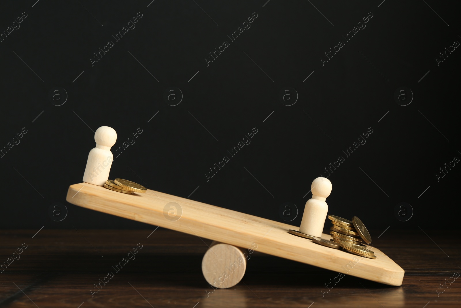 Photo of Financial inequality. Wooden figure with more coins overweighting on scales against black background