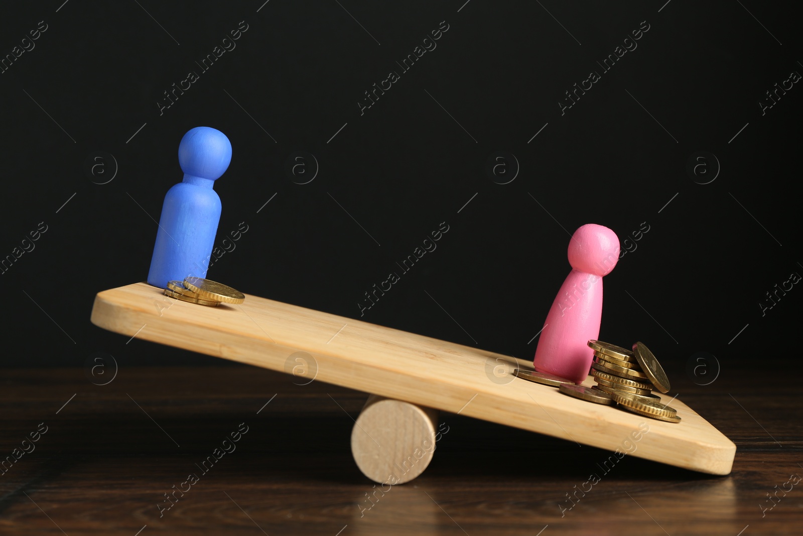 Photo of Financial inequality. Male and female figures with different amount of coins showing imbalance on scales on wooden table