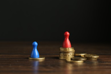 Financial inequality. Male and female figures with uneven amount of coins on wooden table against black background