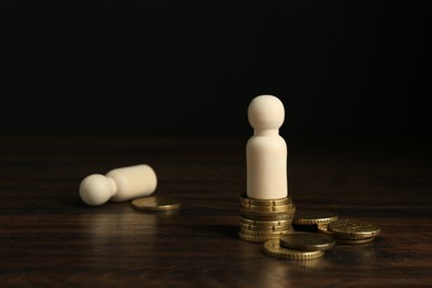 Financial inequality. Wooden figures with uneven amount of coins on table