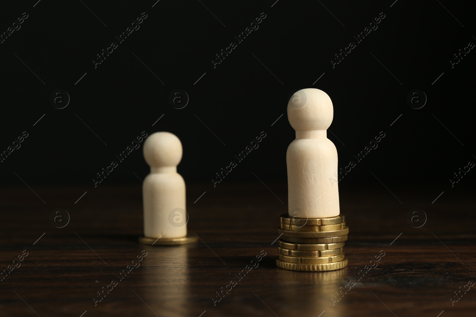 Photo of Financial inequality. One wooden figure with bigger stack of coins than others on table