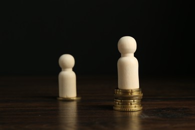 Financial inequality. One wooden figure with bigger stack of coins than others on table