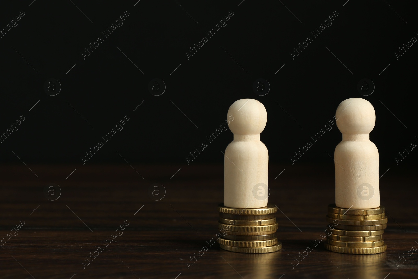 Photo of Financial equality. Wooden figures with stacked coins on table. Space for text