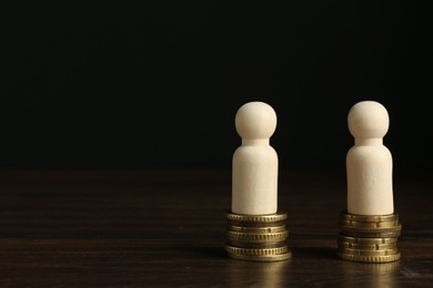 Photo of Financial equality. Wooden figures with stacked coins on table. Space for text